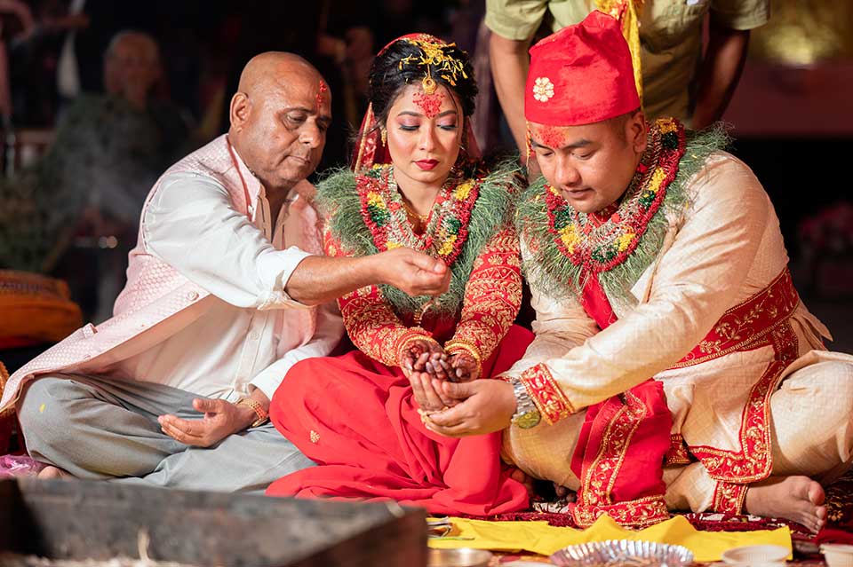 Nepali bride in a red saree and groom in a cream coat, performing marriage rituals in Jalpaiguri, Traditional wedding customs, Groom applying sindoor, Bride and groom play the ring-searching game, Nepali wedding traditions, Nepali Wedding Moments, Best Nepali wedding photographer in Jalpaiguri.
